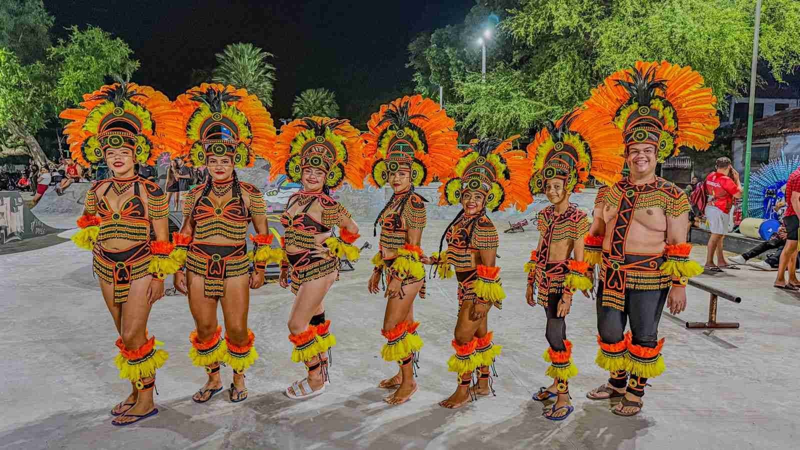 Grupo de danÃ§arinas com cocares laranjas e trajes detalhados